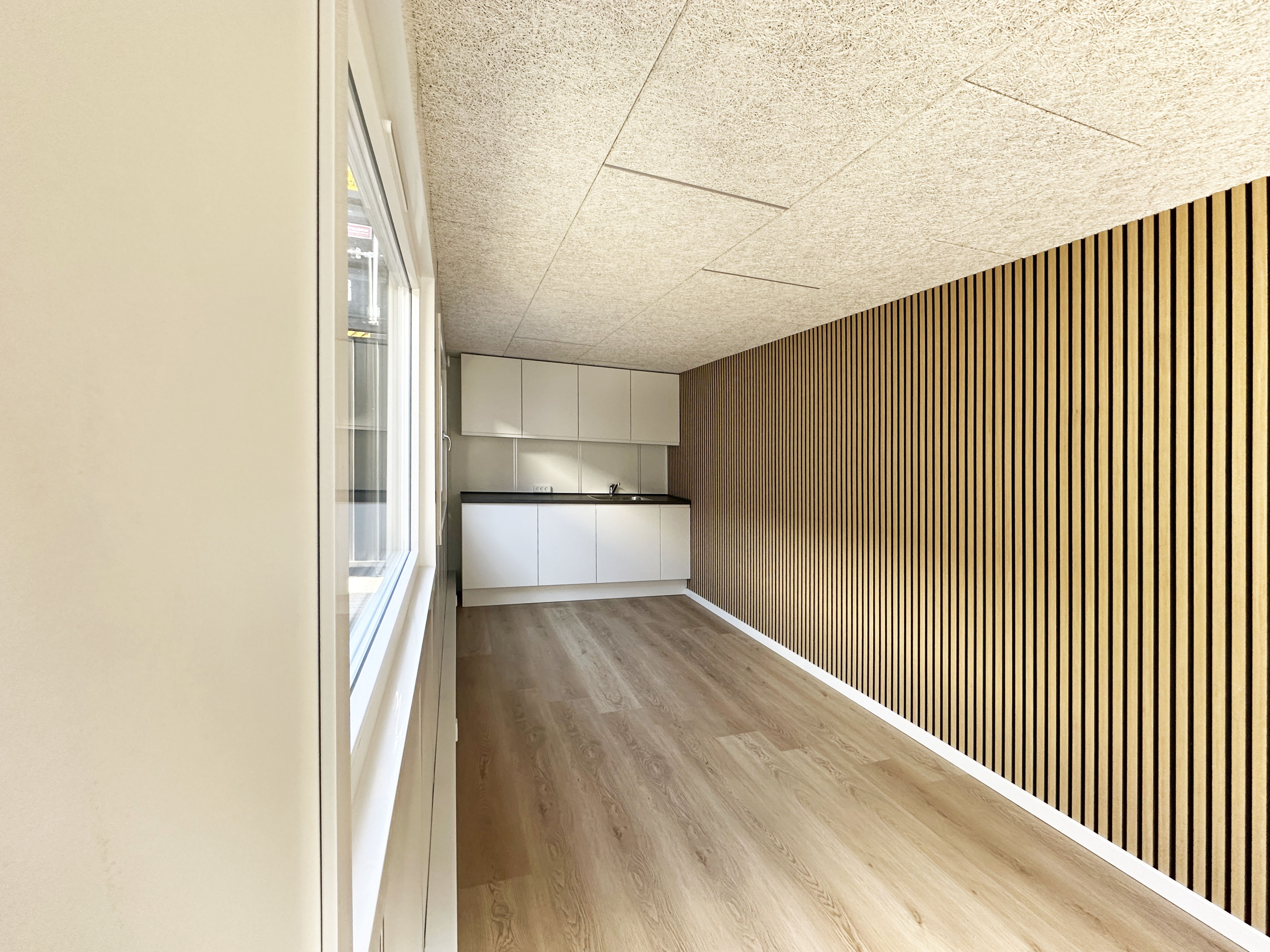 Inredd kontorscontainer med kök, laminatgolv och akustikpanel